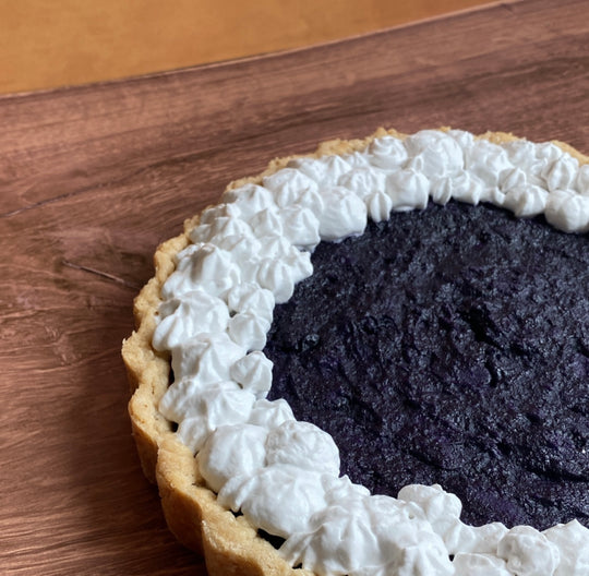 ube pie angled to the right. it's made of a light brown flaky crust, creamy ube filling, with coconut whipped cream adorned all around the outline of the pie
